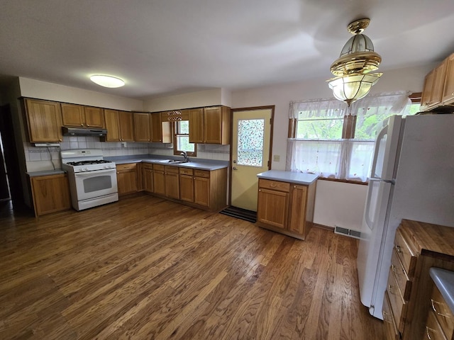 kitchen with brown cabinets, dark wood-type flooring, visible vents, white appliances, and under cabinet range hood