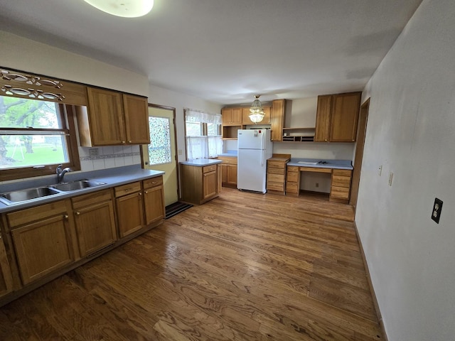 kitchen with a sink, freestanding refrigerator, open shelves, brown cabinetry, and dark wood finished floors