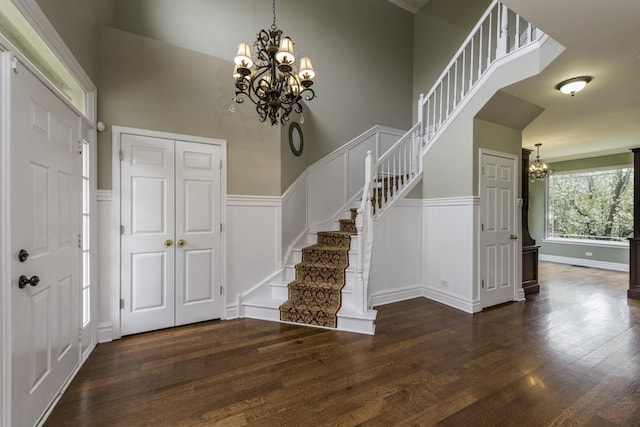 foyer entrance with a chandelier, a decorative wall, wood finished floors, stairs, and wainscoting