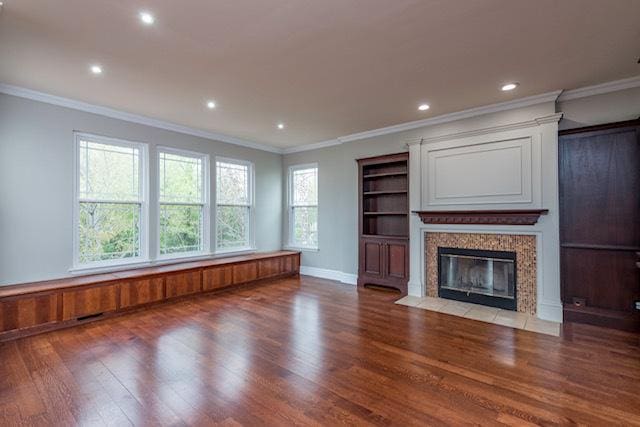 unfurnished living room with wood finished floors, ornamental molding, plenty of natural light, recessed lighting, and a fireplace