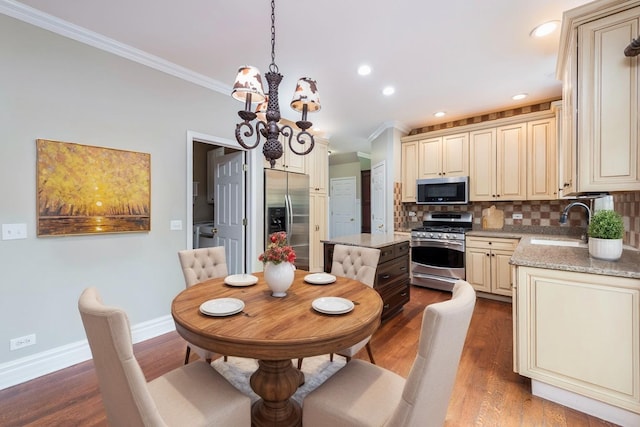 kitchen with stainless steel appliances, cream cabinets, ornamental molding, a chandelier, and a sink