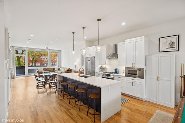 kitchen with appliances with stainless steel finishes, a sink, wall chimney range hood, a kitchen bar, and open floor plan