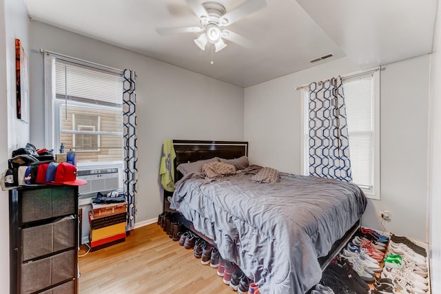bedroom with light wood finished floors, visible vents, ceiling fan, and cooling unit