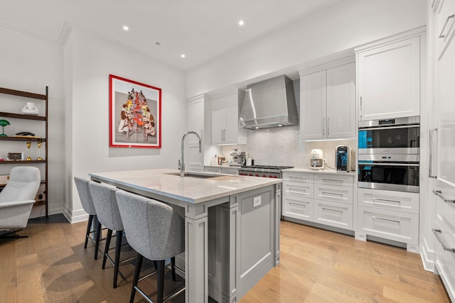 435 N Michigan Ave Unit 416, Chicago, IL 60611 - kitchen with wall chimney exhaust hood, a sink, light wood-style flooring, a center island with sink, and ornamental molding