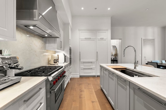 435 N Michigan Ave Unit 416, Chicago, IL 60611 - kitchen featuring wall chimney exhaust hood, stainless steel stove, a sink, light countertops, and light wood-style floors