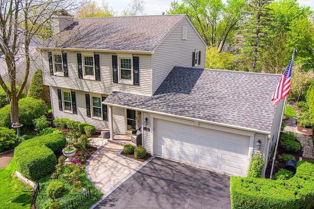 view of front of home featuring a chimney, asphalt driveway, a shingled roof, and a garage