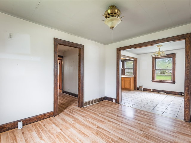 empty room with baseboards, visible vents, light wood-style flooring, and a chandelier