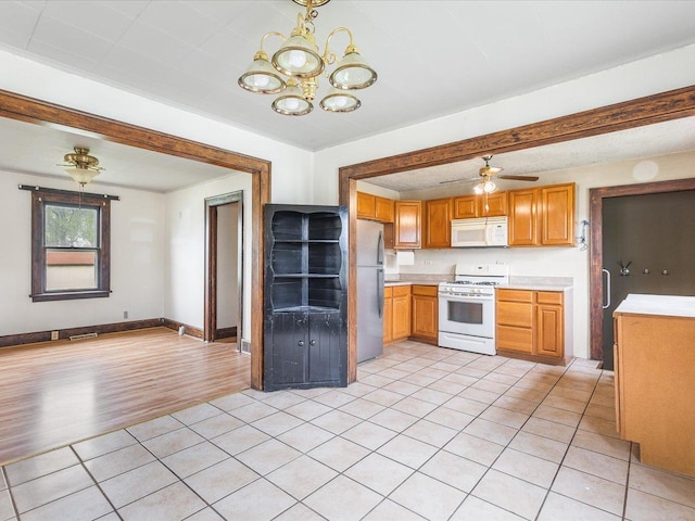 kitchen featuring light tile patterned floors, brown cabinetry, baseboards, white appliances, and light countertops