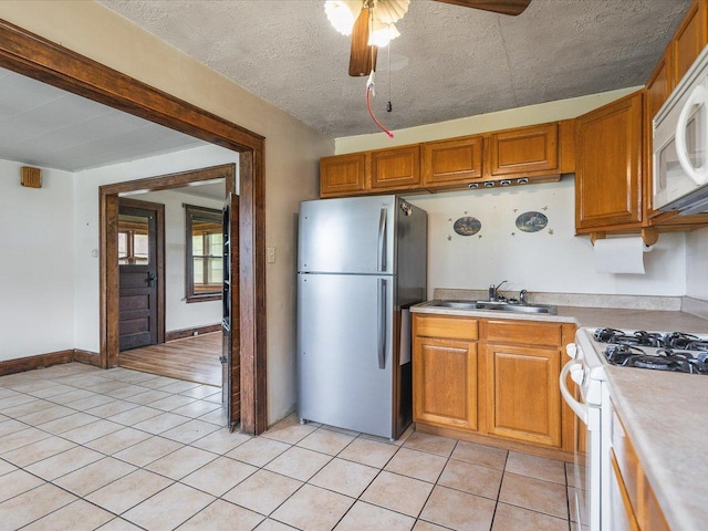 kitchen with brown cabinetry, a ceiling fan, a sink, and white appliances