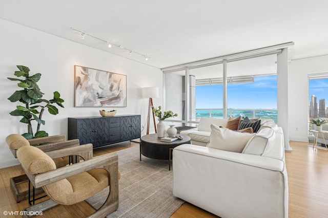 living room with light wood-style flooring, rail lighting, floor to ceiling windows, and a water view