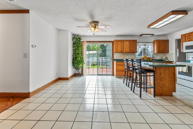 2503 Maplewood Dr, Champaign, IL 61821 - kitchen featuring white appliances, healthy amount of natural light, brown cabinets, a breakfast bar area, and a textured ceiling