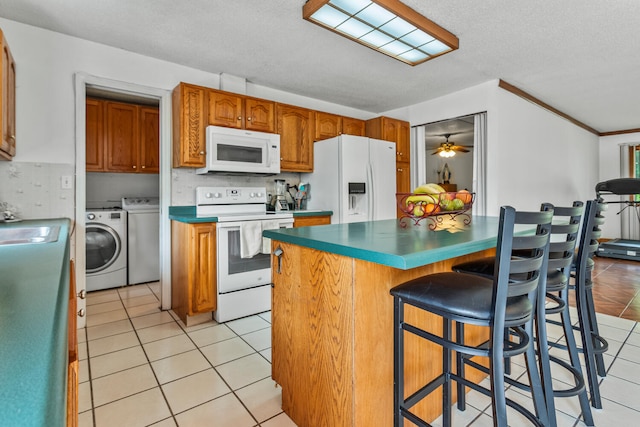 2503 Maplewood Dr, Champaign, IL 61821 - kitchen featuring white appliances, washing machine and clothes dryer, light tile patterned floors, a breakfast bar, and brown cabinets