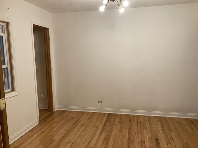 unfurnished room featuring an inviting chandelier, a textured ceiling, baseboards, and light wood-type flooring