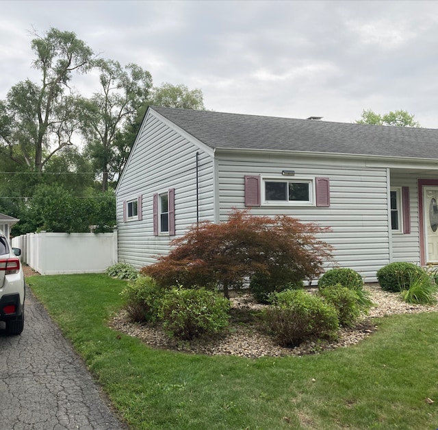 view of property exterior with a lawn, a shingled roof, and fence
