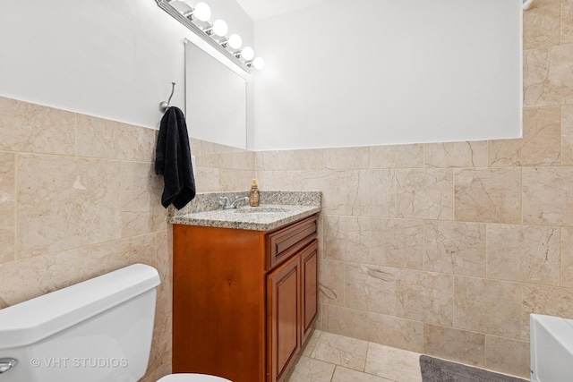 bathroom featuring tile walls, toilet, vanity, a tub to relax in, and tile patterned flooring