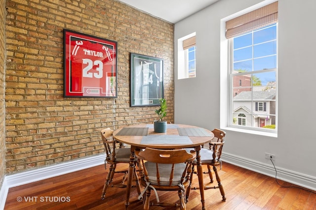 dining area featuring baseboards, hardwood / wood-style flooring, and brick wall