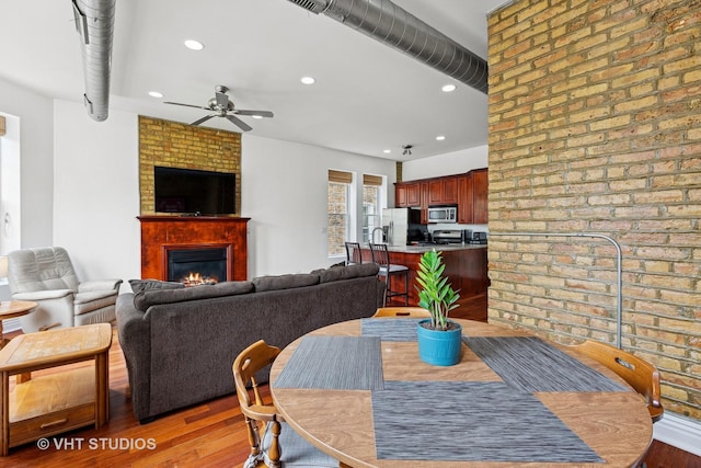 dining space with a ceiling fan, light wood-style flooring, a fireplace, recessed lighting, and brick wall