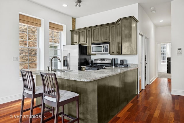 kitchen with stainless steel appliances, a sink, light stone countertops, dark wood-style flooring, and healthy amount of natural light