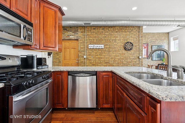 kitchen with appliances with stainless steel finishes, a sink, dark wood finished floors, and light stone countertops