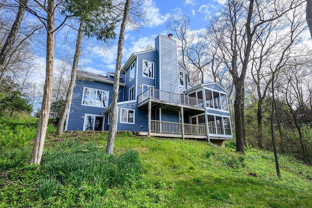 rear view of house with a sunroom, a chimney, a deck, and a balcony