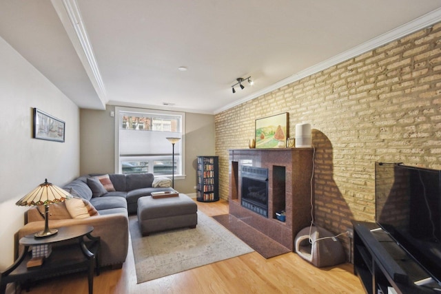 living area with a fireplace with flush hearth, wood finished floors, crown molding, and brick wall