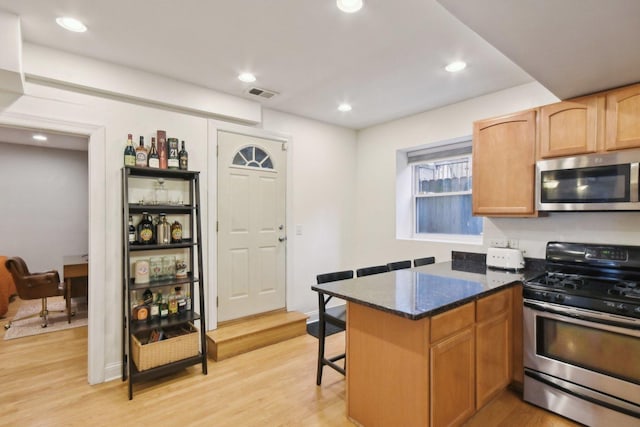kitchen with appliances with stainless steel finishes, light wood-type flooring, a breakfast bar, dark stone countertops, and a peninsula