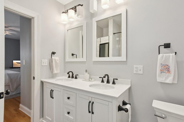 ensuite bathroom featuring toilet, double vanity, and wood finished floors