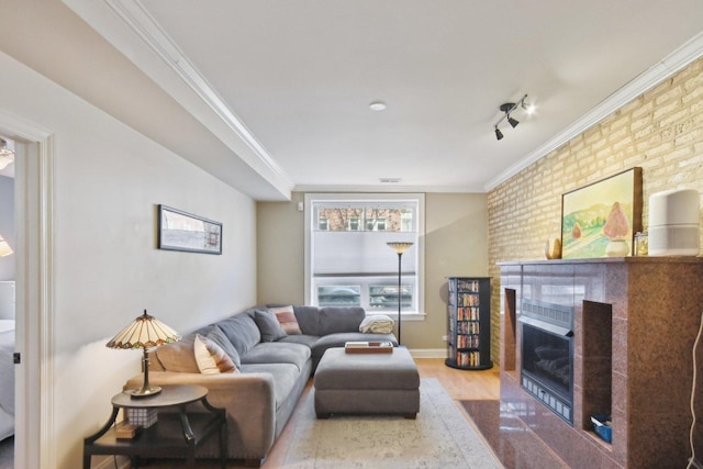 living area featuring wood finished floors, a fireplace, ornamental molding, baseboards, and brick wall