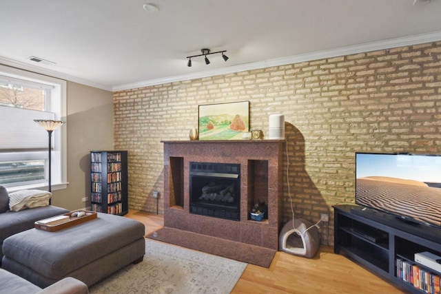 living room with a fireplace, brick wall, wood finished floors, and crown molding