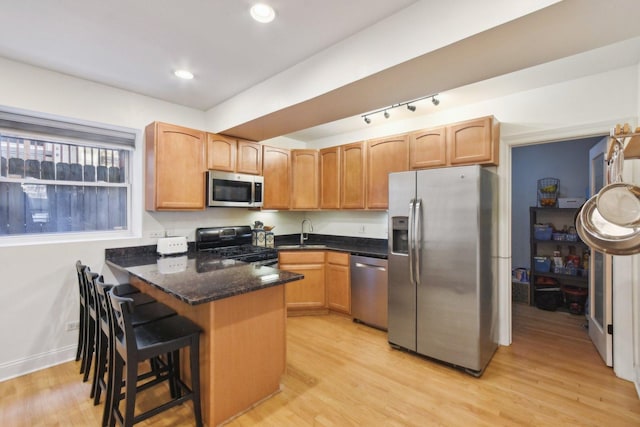 kitchen featuring stainless steel appliances, a peninsula, light wood-style floors, dark stone counters, and a kitchen breakfast bar
