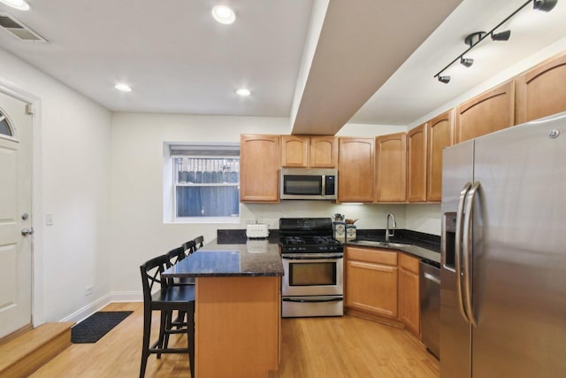 kitchen with appliances with stainless steel finishes, a sink, light wood-type flooring, a kitchen breakfast bar, and a peninsula