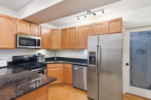 kitchen with appliances with stainless steel finishes, a sink, dark stone counters, and light wood-style flooring
