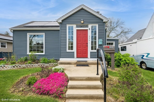 view of front of house with roof mounted solar panels and a front lawn