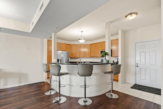 kitchen with a breakfast bar area, stainless steel fridge, wood finished floors, dark countertops, and visible vents