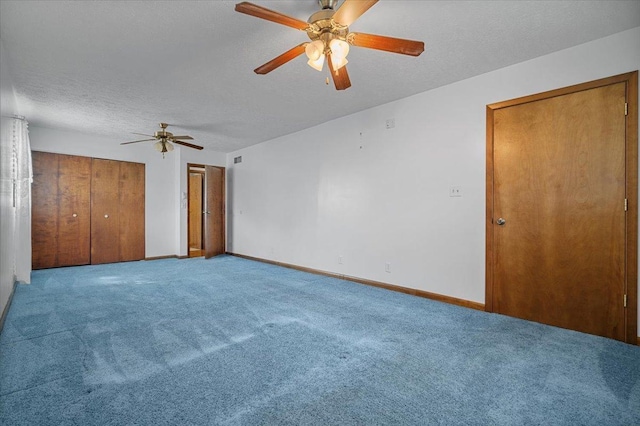 unfurnished bedroom featuring carpet flooring, baseboards, a textured ceiling, ceiling fan, and two closets
