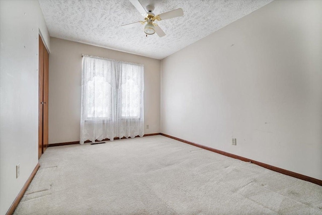 carpeted empty room featuring a textured ceiling, a ceiling fan, and baseboards