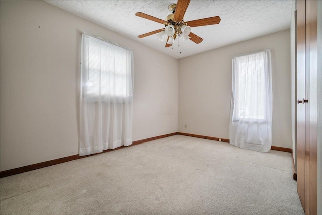 carpeted empty room featuring healthy amount of natural light, a ceiling fan, baseboards, and a textured ceiling