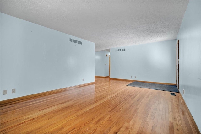 empty room featuring wood-type flooring, a textured ceiling, and baseboards
