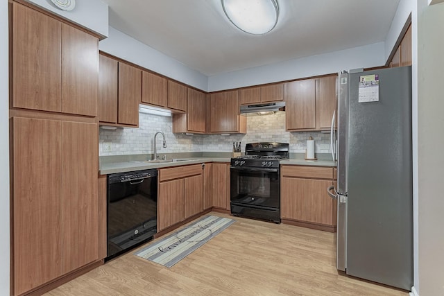 kitchen featuring black appliances, under cabinet range hood, a sink, light wood-type flooring, and tasteful backsplash