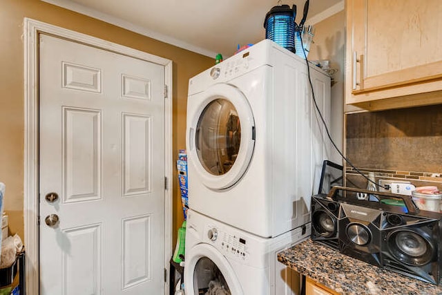 washroom with cabinet space, stacked washing maching and dryer, and ornamental molding