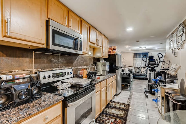 kitchen featuring a sink, open floor plan, decorative backsplash, stainless steel appliances, and dark stone counters
