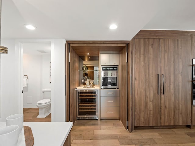 indoor bar with wine cooler, light wood-style flooring, and recessed lighting