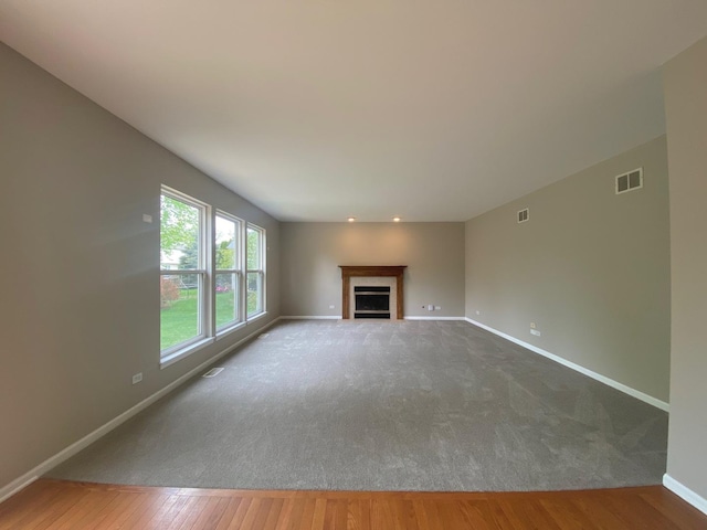 unfurnished living room featuring carpet, baseboards, visible vents, wood finished floors, and a fireplace