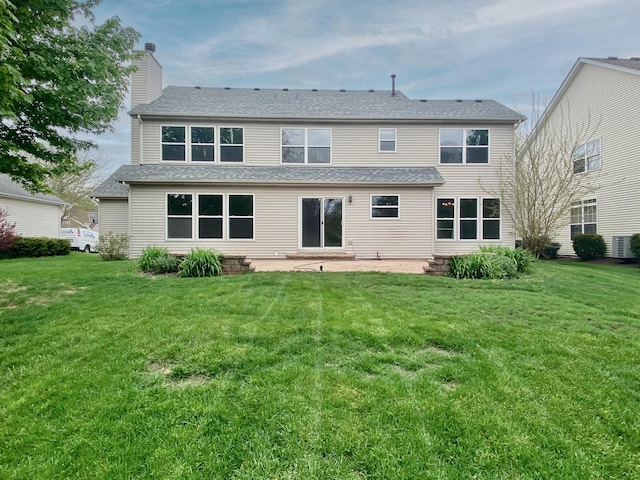 back of property featuring roof with shingles, a patio, a chimney, and a lawn