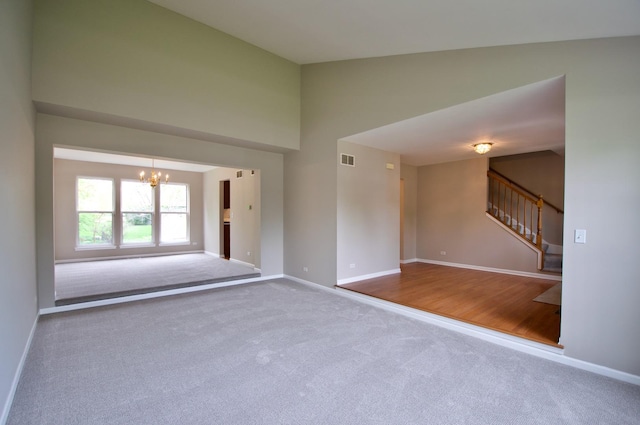 spare room featuring a notable chandelier, carpet, baseboards, visible vents, and stairway