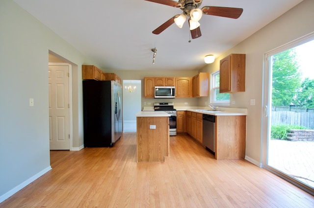 kitchen featuring stainless steel appliances, a sink, a kitchen island, light wood-style floors, and light countertops