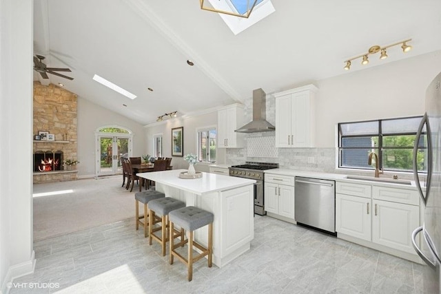 kitchen with appliances with stainless steel finishes, a skylight, wall chimney exhaust hood, a sink, and a center island