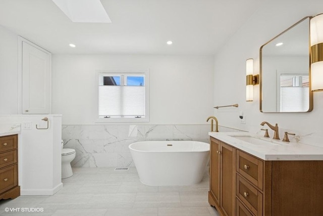 bathroom featuring tile walls, a soaking tub, vanity, a skylight, and wainscoting