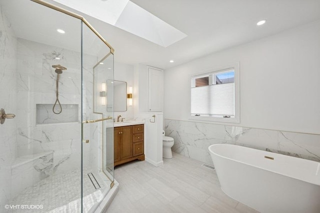 bathroom featuring a skylight, a marble finish shower, vanity, a freestanding bath, and toilet