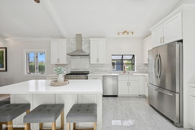 kitchen featuring appliances with stainless steel finishes, wall chimney exhaust hood, a sink, plenty of natural light, and ornamental molding
